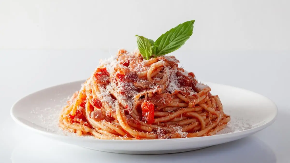 Spaghetti med tomatsås, parmesan och ett grönt basilikablad på en vit tallrik